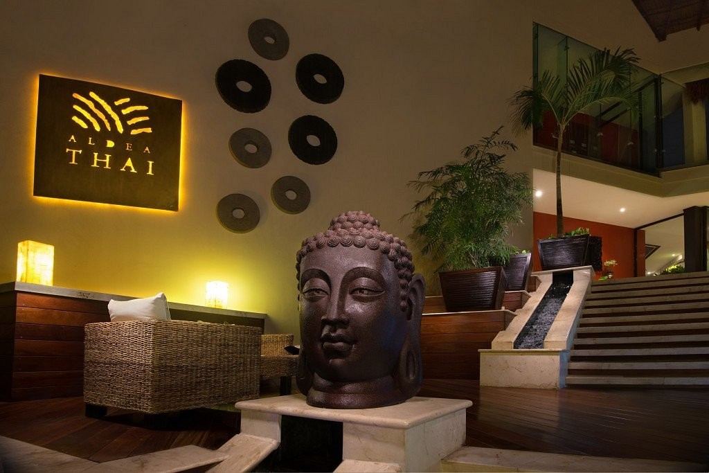 A bronze Buddha and the lit Aldea Thai sign in the lobby
